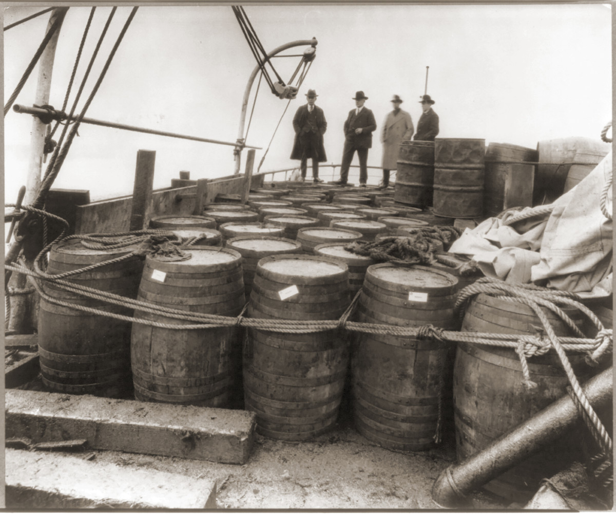 Agents examining barrels on the deck of a ship.